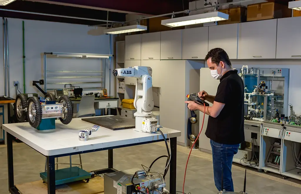 Engenheiro usando controle remoto para operar um braço robótico em um laboratório de pesquisa.